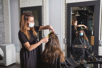 Mujer estilista corta el pelo a mujer clienta, con la mascarilla puesta de protección ante el...