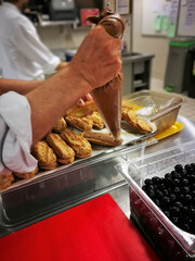 Close up of professional chef hands filling french dessert eclairs with chocolate filling. Food