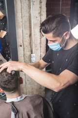 Peluquero cortando el pelo a cliente, ambos con la mascarilla de protección por el virus COVID19