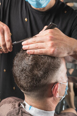 Peluquero cortando el pelo a cliente, ambos con la mascarilla de protección por el virus COVID19