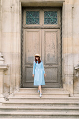 Fototapeta na wymiar Photo of a beautiful young woman in blue dress descends the vintage stairs on the background of old building with doors