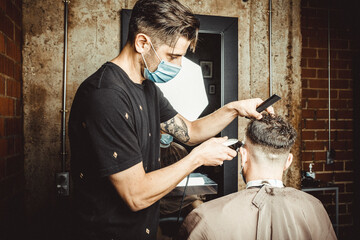 Peluquero cortando el pelo a cliente, ambos con la mascarilla de protección por el virus COVID19