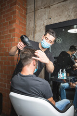 Peluquero cortando el pelo a cliente, ambos con la mascarilla de protección por el virus COVID19