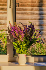 A bouquet of violet wildflowers lit by sunlight in a farmhouse.