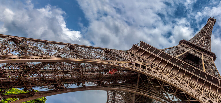 Wide angle artistic panoramic photo of the Eiffel Tower in Paris looking up to sky with broken clouds
