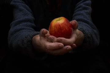 Grandma gives an apple. Grandmother holds an apple in both hands. Low key.
