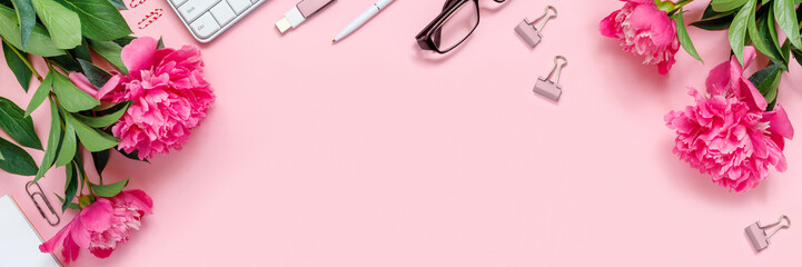 Laptop, accessories and bouquet of beautiful peonies with glasses and headphones on pink background. Flat lay of working place.