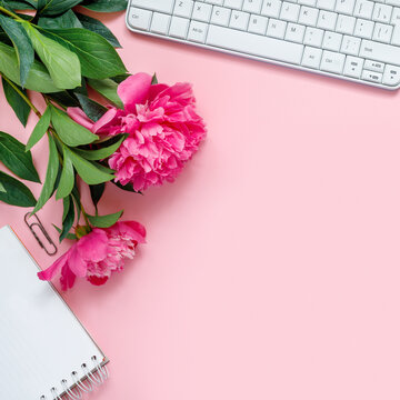 Laptop, accessories and bouquet of beautiful peonies on pink background. Flat lay of working place.