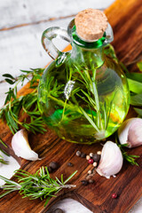 Flavored fresh naturalolive oil with herbs: rosemary, sage, thyme, garlic, pepper in glass bottle on wooden board. Wooden background, close up. Mediterranean cuisine, ideal salad dressing.