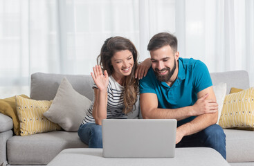 Young couple man and woman talking online over the laptop to her parents first time from their new apartment after they finally moved out from his parents  house