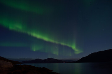 Naklejka na ściany i meble mighty aurora borealis dancing on night sky over mountain and fjord landscape in late autumn in the arctic circle
