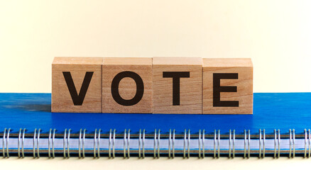 VOTE word written on wooden blocks black font on background blu notepad. Vote word on four wood cube dices on white grey glossy background.