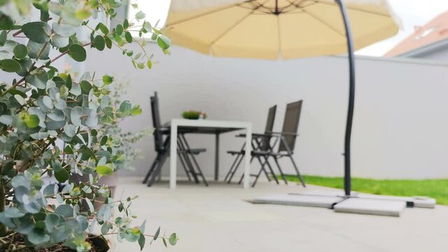 Cozy modern terrace with table and sunshade and eucalyptus bush on foreground