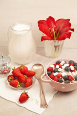Breakfast with strawberries, blueberries and raspberries with flakes, milk decorated with red amaryllis.