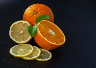Fototapeta na wymiar fresh juicy oranges and lemons on a black background with water drops