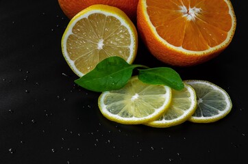fresh juicy oranges and lemons on a black background with water drops