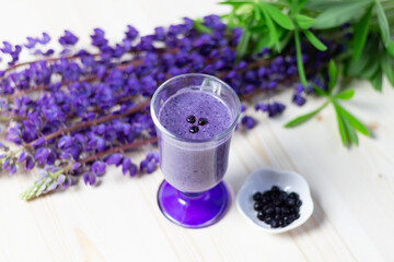 glass of fresh banana and blueberry smoothie and purple lupine flowers on wooden table