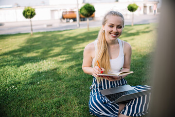 Cheerful woman browsing internet and taking notes in city