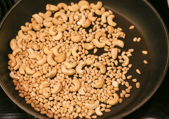 Cashew nuts and pine nuts roasted in black cast-iron pan directly above view