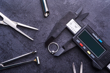 Electronic caliper with piercing earring and clips. Lying on a black background. Piercing theme