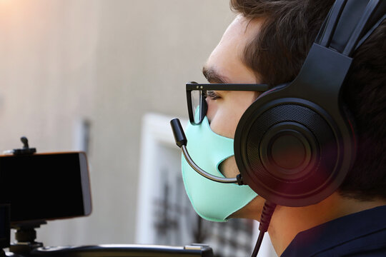 Closeup photography of a videographer working outdoor,with headphones and microphone.Face mask as protection from covid on the face.
