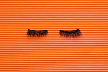 Black false lashes strips on orange textured background