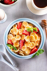 Trendy home breakfast with tiny cereal pancakes with honey and strawberries in the bowl. Top view