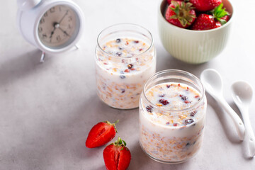 Granola, yogurt and strawberries in a jars on the light background with alarm clock. Copy space.