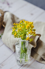 Home interior decor, freshly picked bouquet. Wild,  yellow flowers in a bottle on the table with vintage cloth in the background 