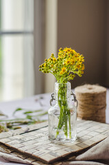 Home interior decor, freshly picked bouquet. Yellow flowers in a bottle on the table with string and window in the background 