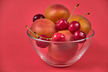Fresh juicy apricots and red sweet cherries in a transparent glass plate. Macro.