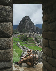 Traveler with a backpack looks at Machu Picchu. Man in a hat looks at an ancient historical site. Indiana Jones reveals the secrets of civilizations. Seven wonders of the world Machu Picchu, Peru.