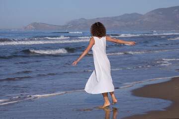 A woman in white dress walking near a beach in hot sunny summer day. High quality photo