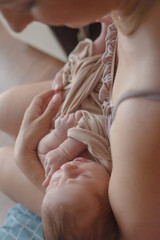 Obraz premium Young mother holding on hands newborn two weeks baby at home in the room. Home portrait of happy fаmily against the window