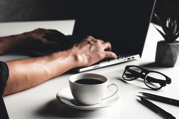 A man types on a laptop, business concept, glasses, a cup of coffee and a pen on a gray background.