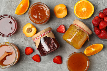 Glass jars with jam and ingredients on gray background, top view