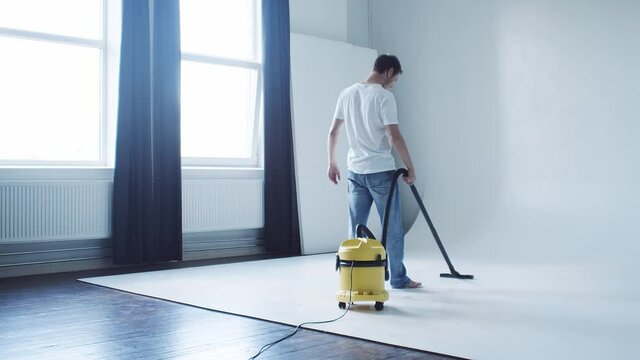 Man cleaning cyclorama in photo studio using vacoom cleaner