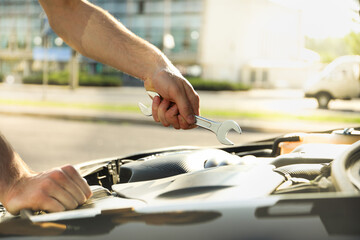 A man holds a wrench over a car engine. Car inspection