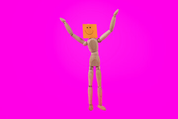 Jointed wooden figure standing holding up arms with a happy smiling face sign on a bright pink background 