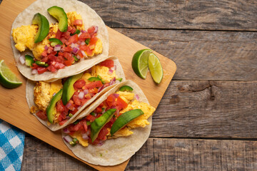 Breakfast egg tacos with flour tortilla and fresh sauce on wooden background