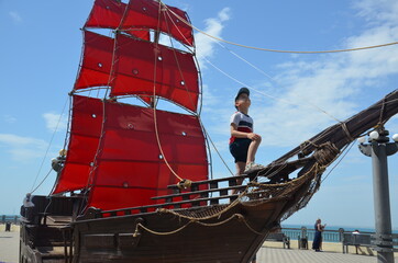 boy looks into the distance on an old ship with red sails. boy under the red sail