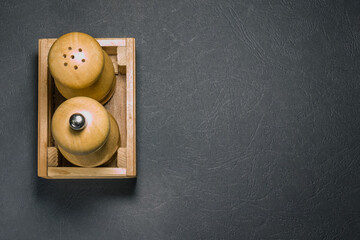 Wooden salt shaker and pepper shaker in box on the left side on black surface