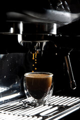 Dark coffee drops dripping in a transparent glass espresso cup on a manual espresso machine with copy space, close up