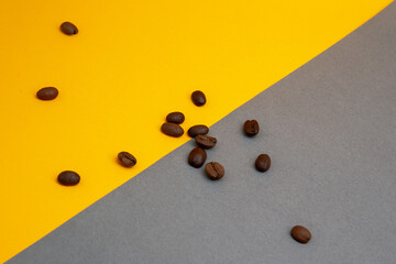 Spilled roasted brown coffee beans isolated on yellow background, close up with copy space