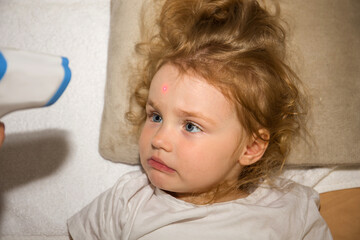 Temperature measurement by a laser thermometer. Little curly redhead girl. Child disease concept