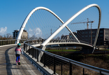 Fototapeta premium A young girl on a scooter on the Peter Courtney Minto Island Bridge, it connects Salem's Riverfront park to Minto Brown Park, Salem, Oregon