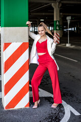 Fototapeta na wymiar young blonde schoolgirl in a red suit and a white jacket posing in the parking lot