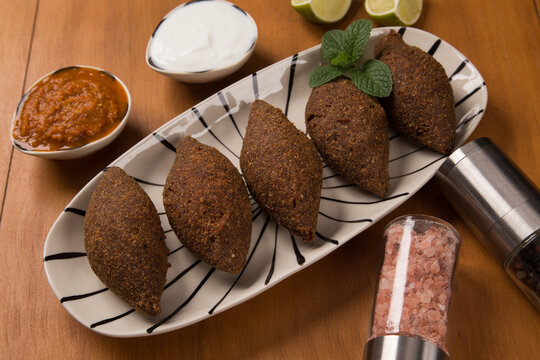 fried kibbeh served with yogurt sauce, and pepper sauce, on a plate