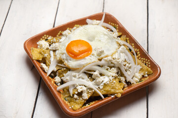 Mexican green chilaquiles with fried egg and cheese on white background
