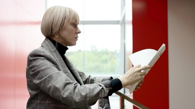 A side view slow motion close up shot of a blonde business woman reading every page of a contract recieved from a business partner